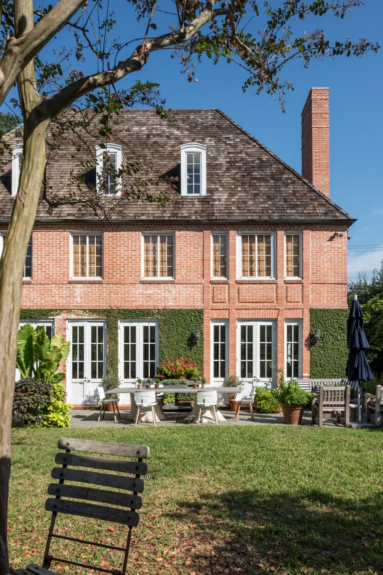 Large two-story house with brick exterior and white trim surrounded by a well-manicured lawn and garden The house features multiple windows a