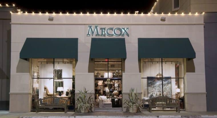 Mecox storefront at night with lit sign and awning