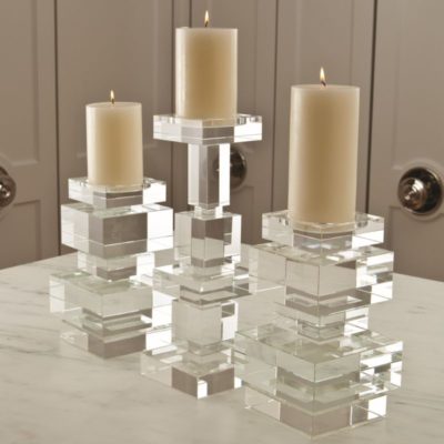 A transparent geometric candle holder with a lit candle on top, displayed on a table.