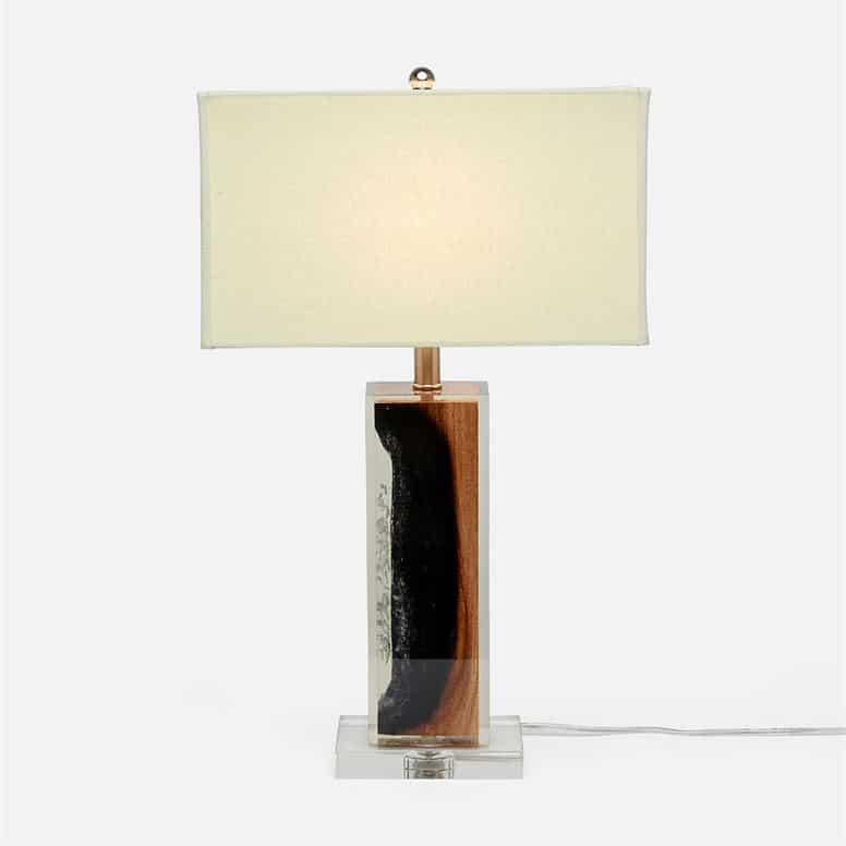 A tall modern table lamp with a unique design featuring burnt raw wood encased in a clear resin cube on a lucite