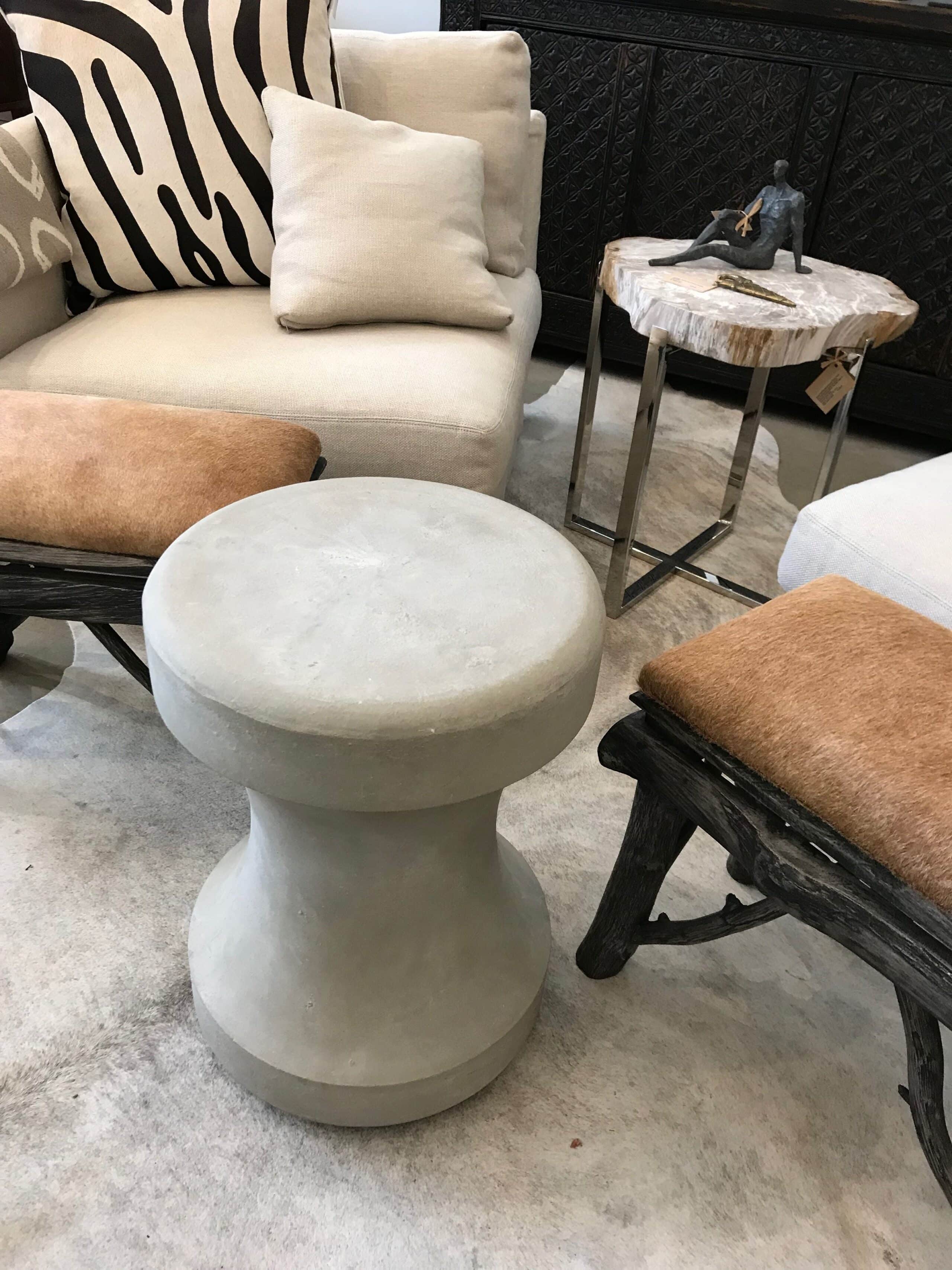 A concrete chess piece stool in a light gray finish sitting on a beige rug in front of a white sofa with