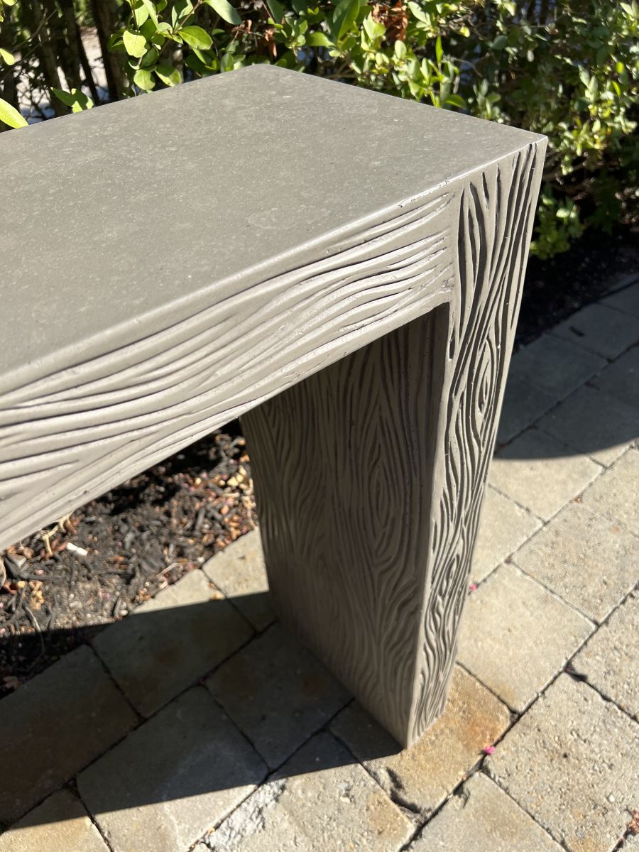 Dark gray concrete console table with etched design, showcasing faux bois texture in outdoor setting.