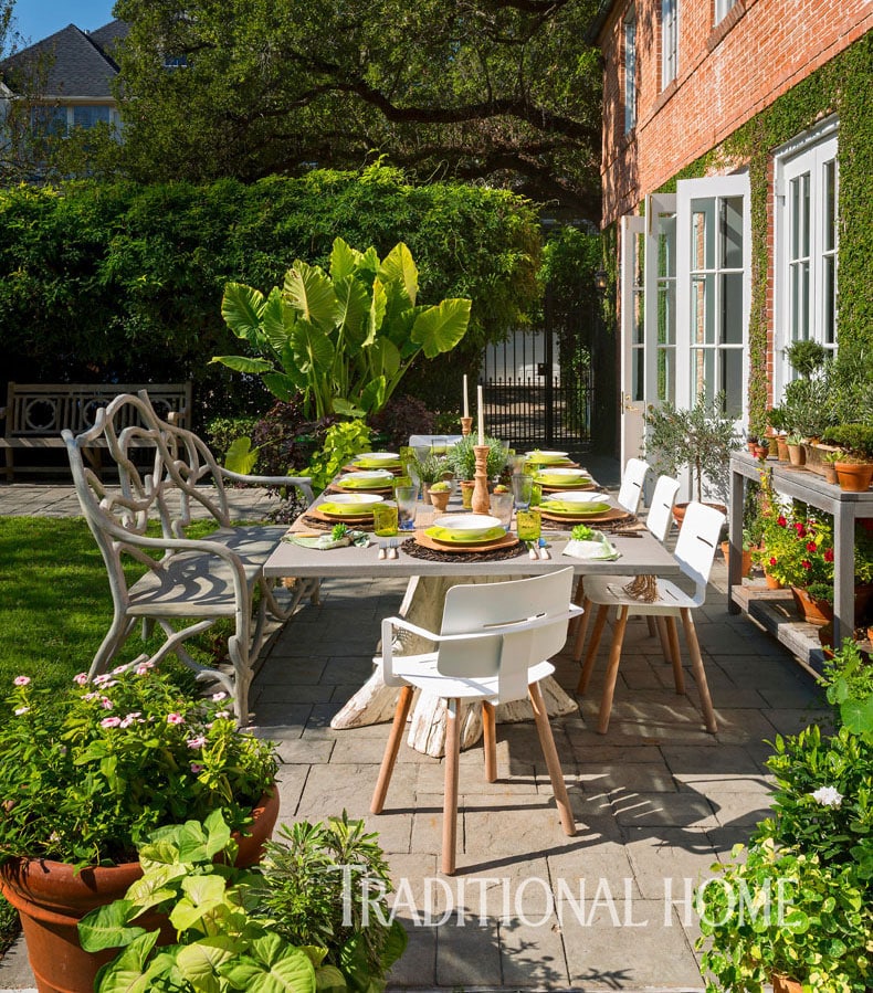 Backyard patio with outdoor dining set, including table and chairs, surrounded by potted plants and a brick wall.
