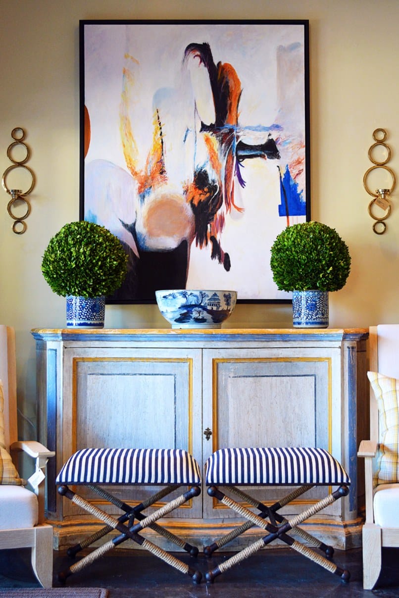 A large framed painting hanging above a bench in an interior space The painting depicts a person with their arms raised To