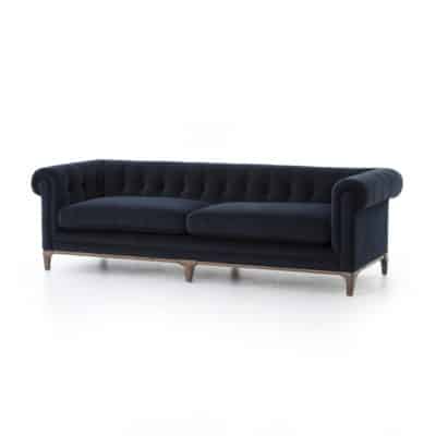 Stylish navy blue velvet sofa with tufted button detailing and wooden base, showcasing its elegant design in a studio setting.