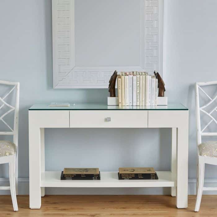 A pair of white chairs with a glass top desk in a room with blue walls and a mirror.