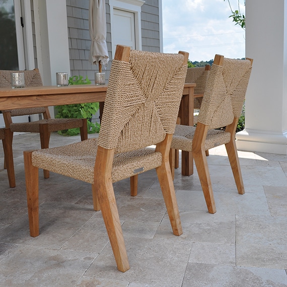 The image shows a set of outdoor teak and rope dining side chairs There are four chairs visible each with a woven