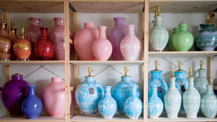 A variety of colorful vases displayed on a wooden shelf against a white wall.