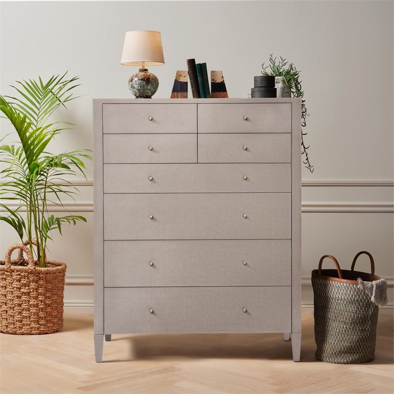 A tall, light-colored dresser with eight drawers and a faux raffia finish, displayed in an indoor setting against a white wall.