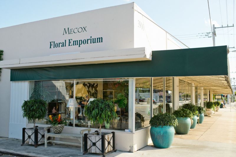 A white building with a green awning that reads mecox floral empire in black lettering The building has multiple windows and a