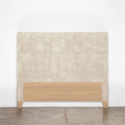 A beige faux shagreen headboard with wooden base against a white wall.