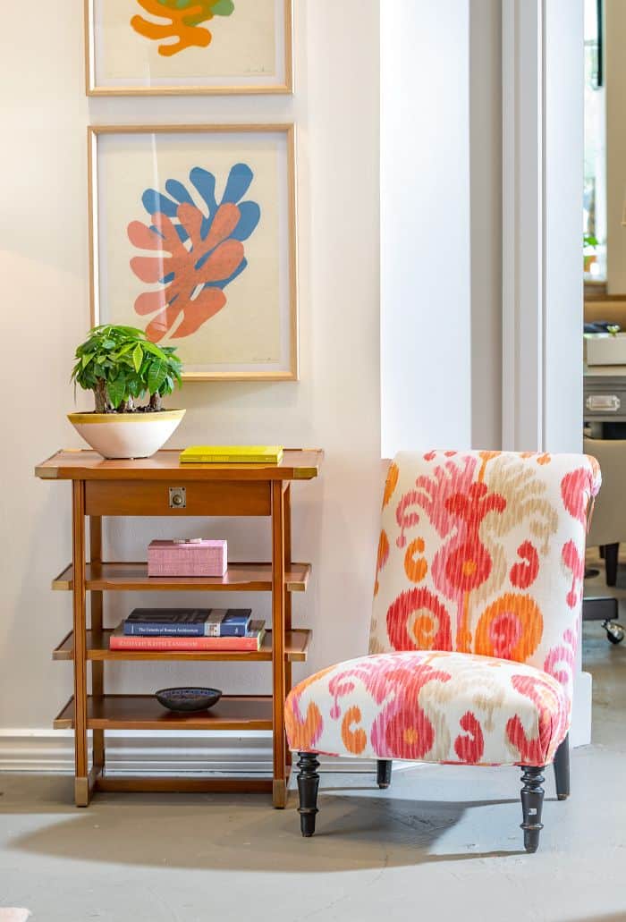 Colorful painting with abstract design in a white frame, displayed on a wall above a chair and table.