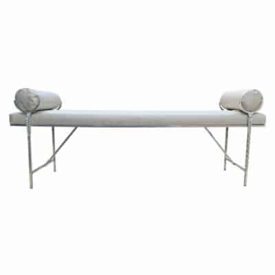 A sleek modern metal bench with a silver finish featuring a textured surface that resembles fabric It has two cushions for added