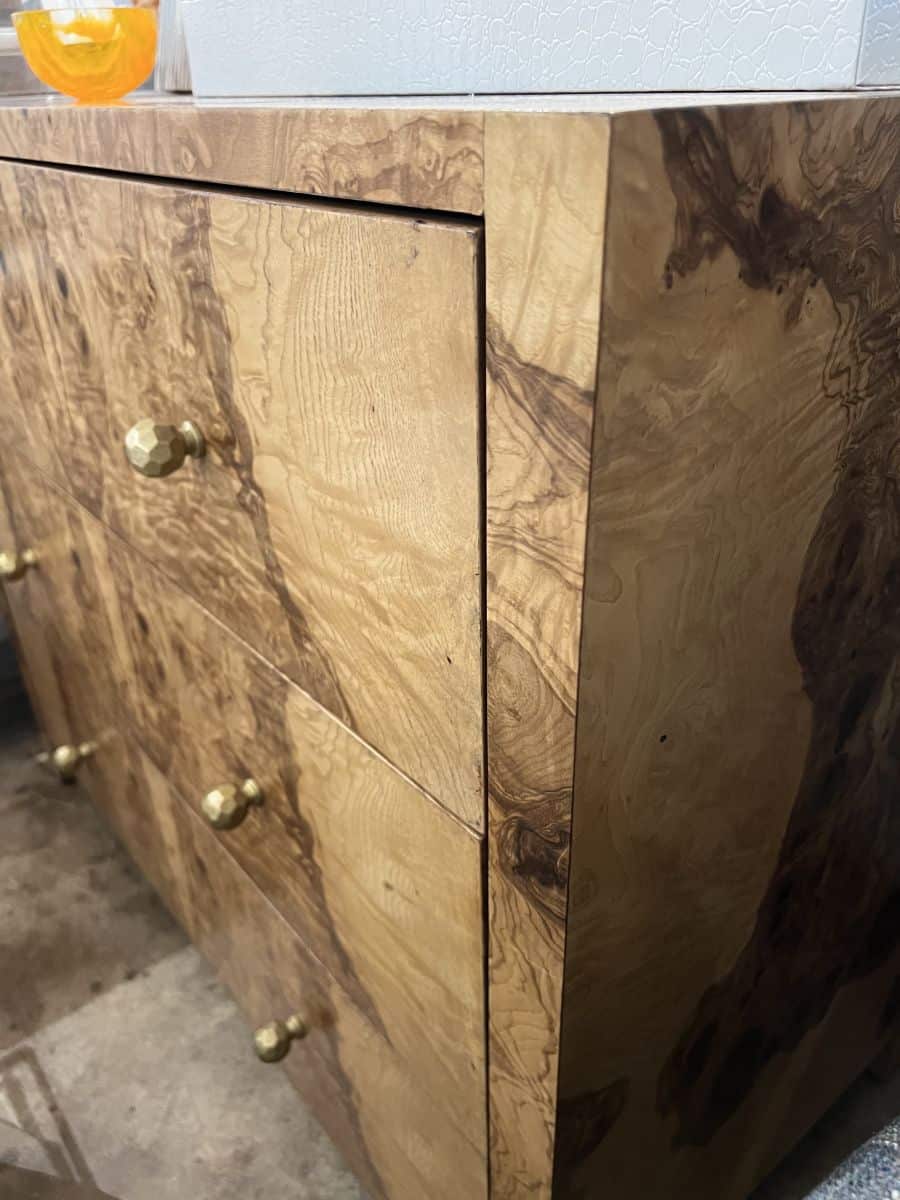 Close-up of a luxurious olive ash veneer dresser featuring brass hardware.