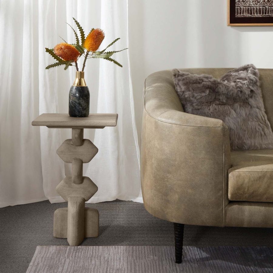 Hand carved mango wood accent table, dark rustic finish, available in light gray, side view with couch and flowers in background.