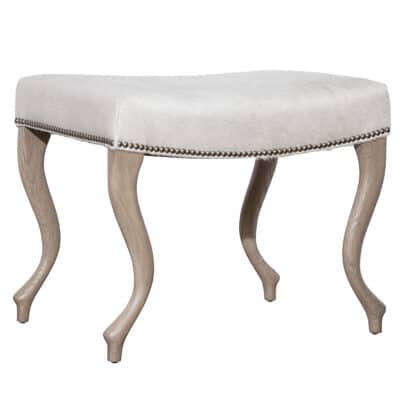 Close-up of Upholstered Hide Ottoman in Serengeti Natural Grade 7 Hide, featuring curved wood legs with platinum nailhead trim.