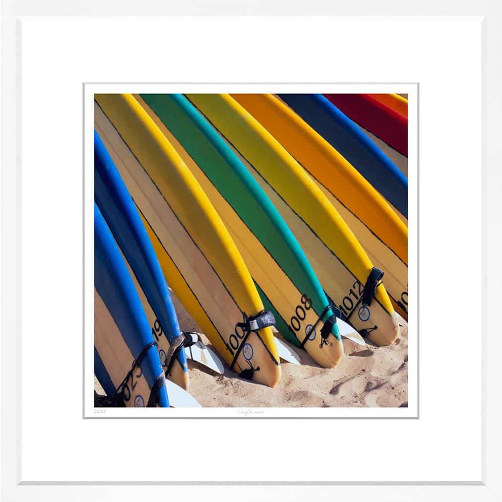 Stacked surfboards in vibrant colors, captured in a striking photograph within a white frame.