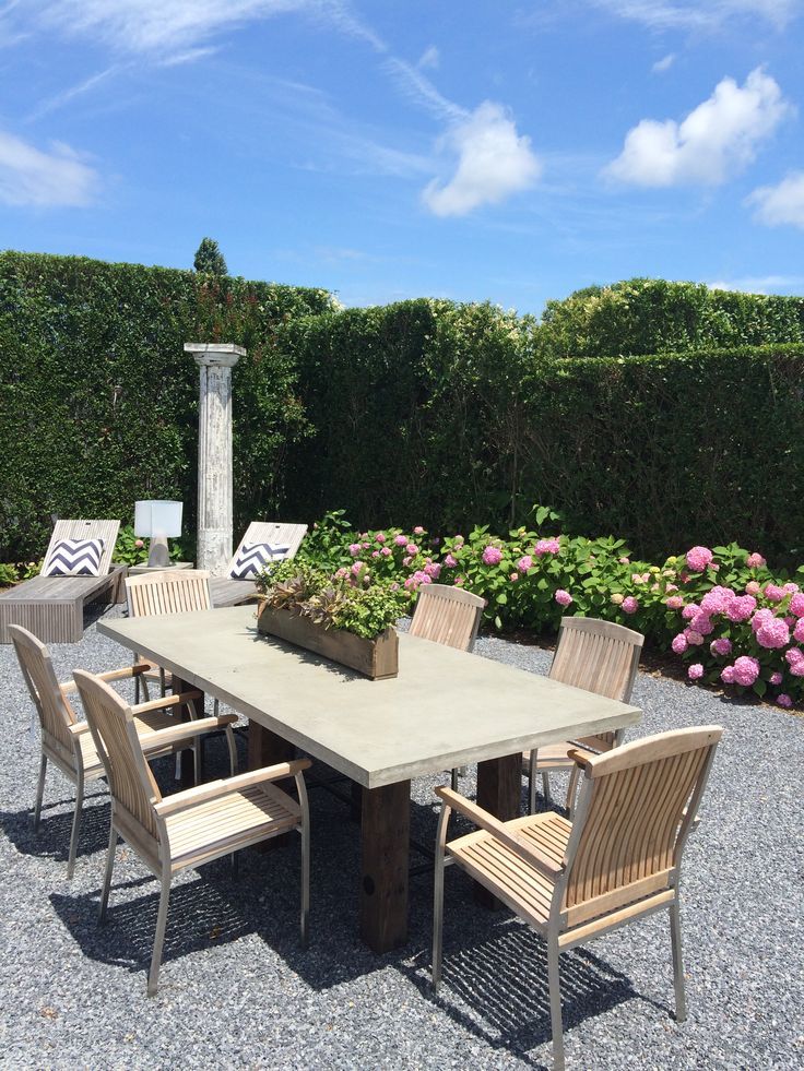 Front view of patio table with light brown wicker chairs, set against a backdrop of lush greenery under clear blue skies.