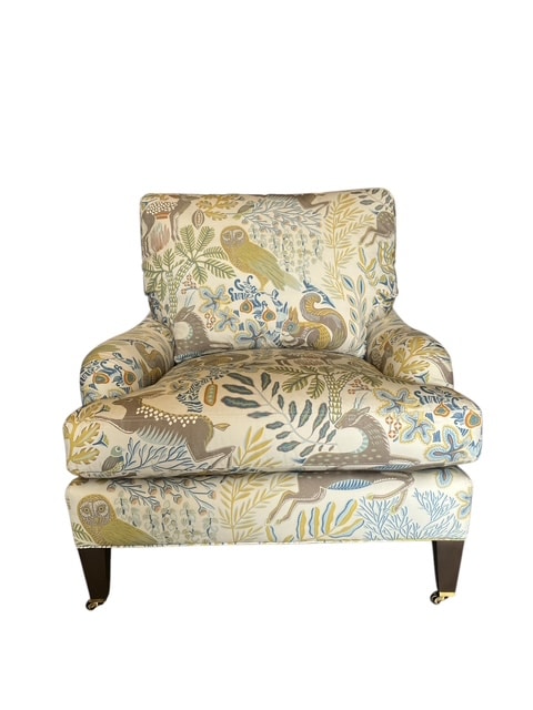 Close-up of Wonderland Fawn Arm Chair upholstered in vibrant patterned fabric, featuring pecan finish wooden legs and brass casters.