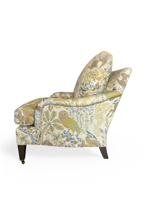 Close-up of Wonderland Fawn Arm Chair featuring ornate upholstery in vibrant floral pattern on wood legs with brass casters.