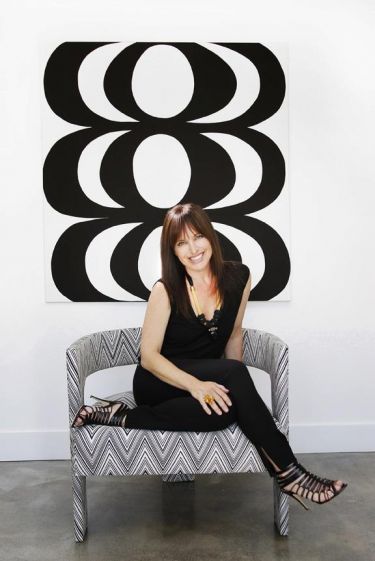 Woman sitting on patterned bench, smiling at camera in front of modern art display featuring bold geometric shapes.