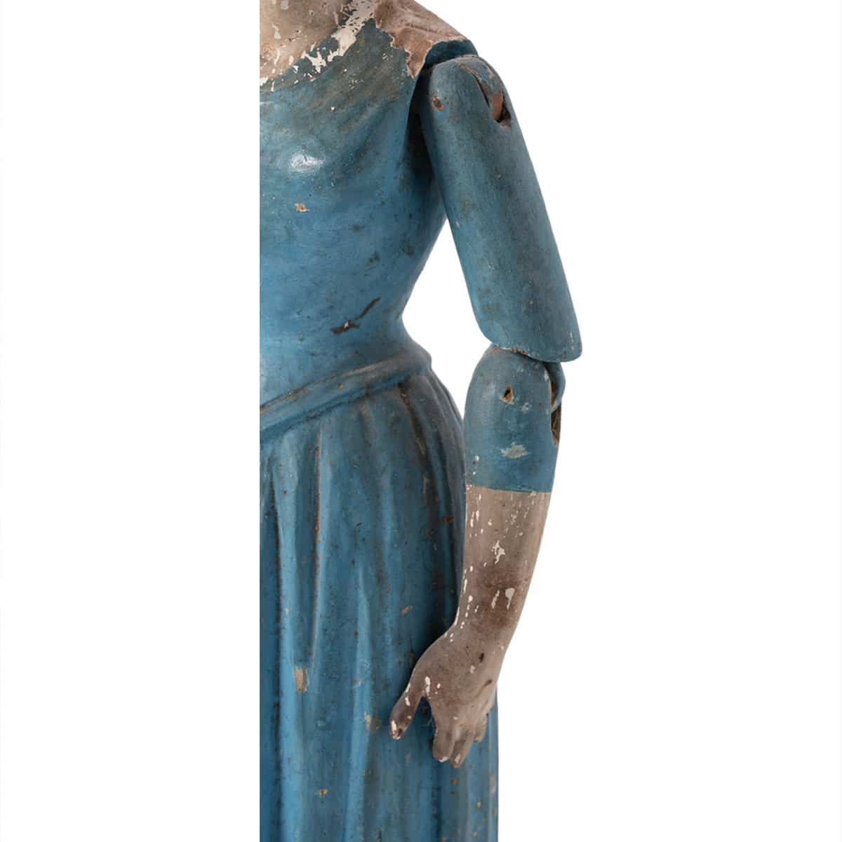 Back view of antique wooden doll with blue dress, arms, and hands in original paint.