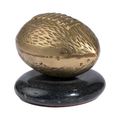 Close-up of brass football paperweight with intricate design on marble base.