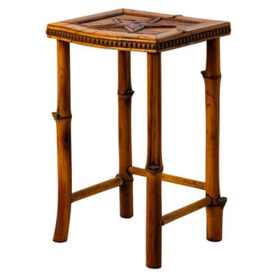 Side view of small vintage drinks table featuring inlaid star decor on top, glass top, and three-sided stretcher connecting three legs.