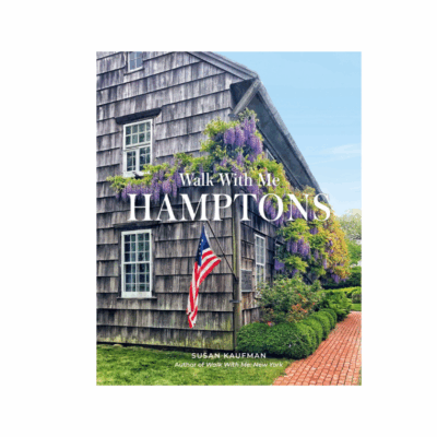 Front view of wooden house with American flag, surrounded by purple flowers.
