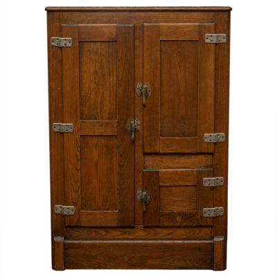 Close-up of an antique oak ice box wood cabinet, featuring three doors with brass hardware and interior shelves, showcasing its vintage charm.