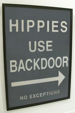 A vintage poster featuring a sign that reads Hippies Use Backdoor in a bold sans-serif font on a blue background The sign