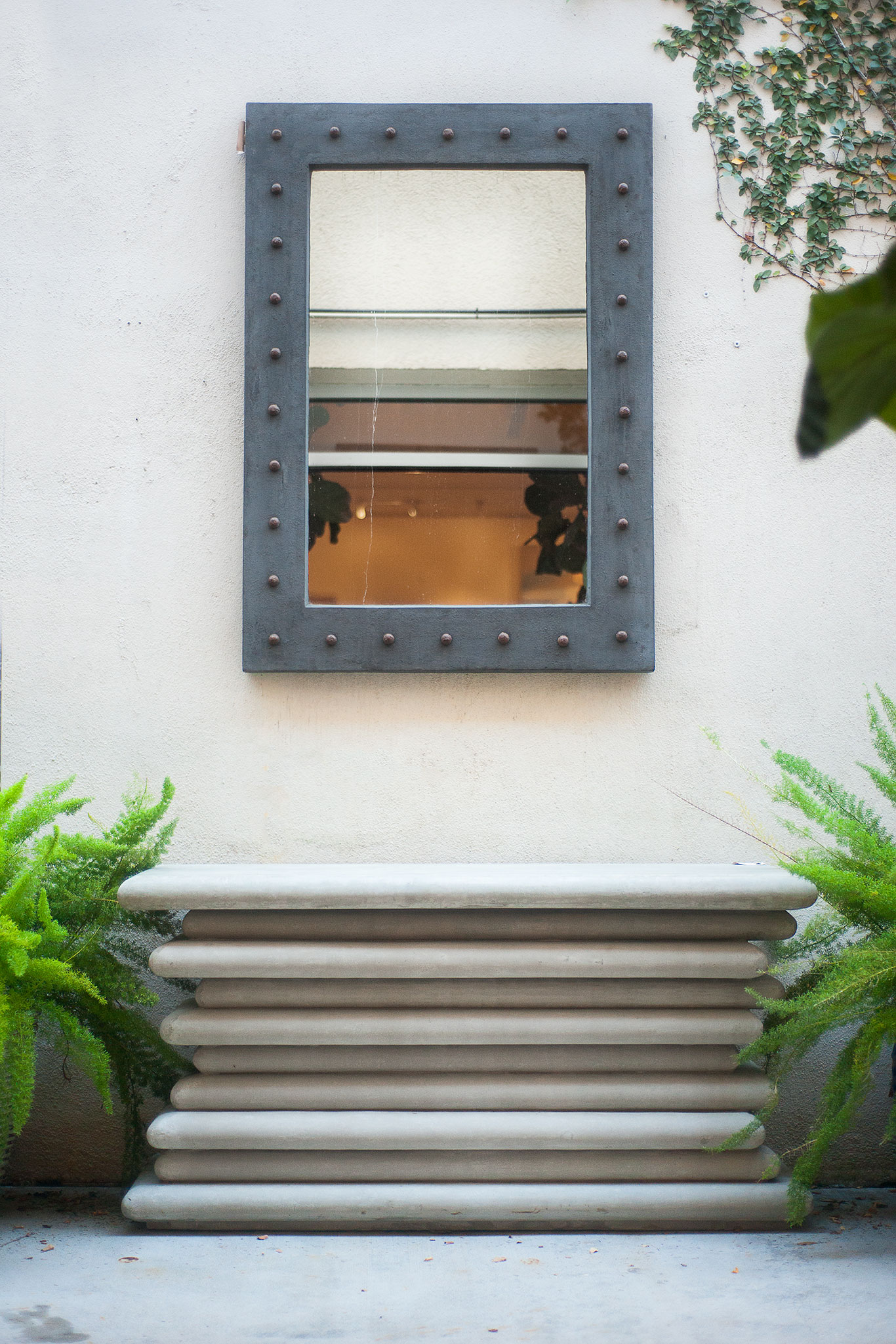A tall light gray outdoor console table with a dark brown rectangular mirror mounted on its front set against a beige wall