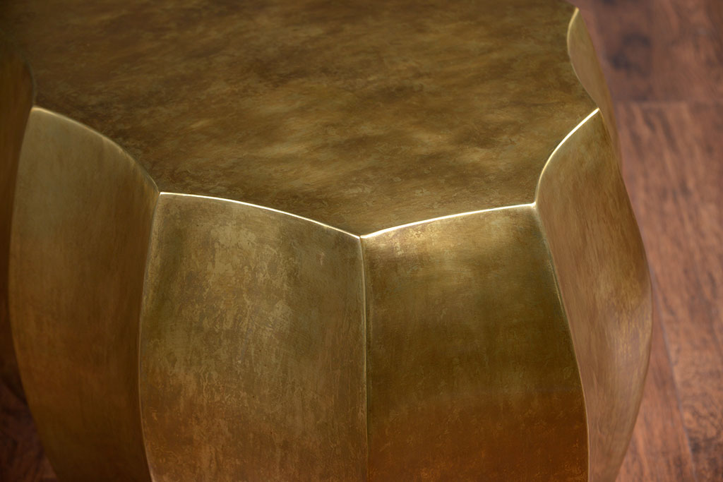 The image showcases a contemporary scalloped antiqued brass oval coffee table It is a large round table with a unique design featuring