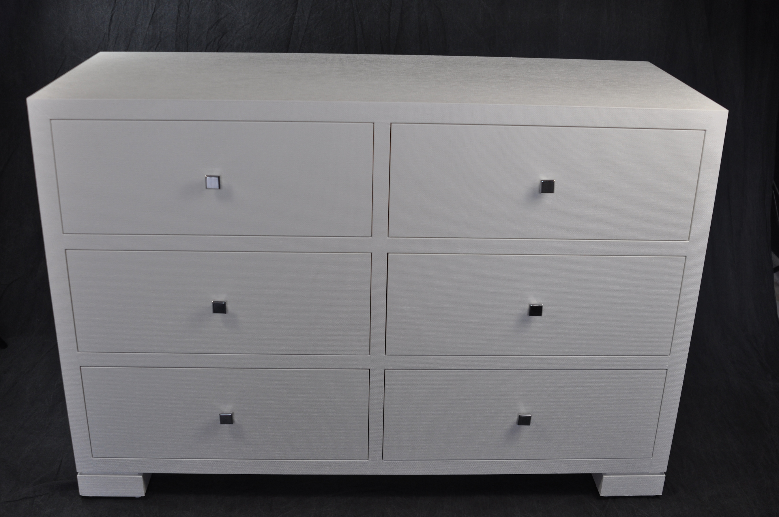 White six drawer dresser with hand-cast chrome handles, displayed in a showroom.