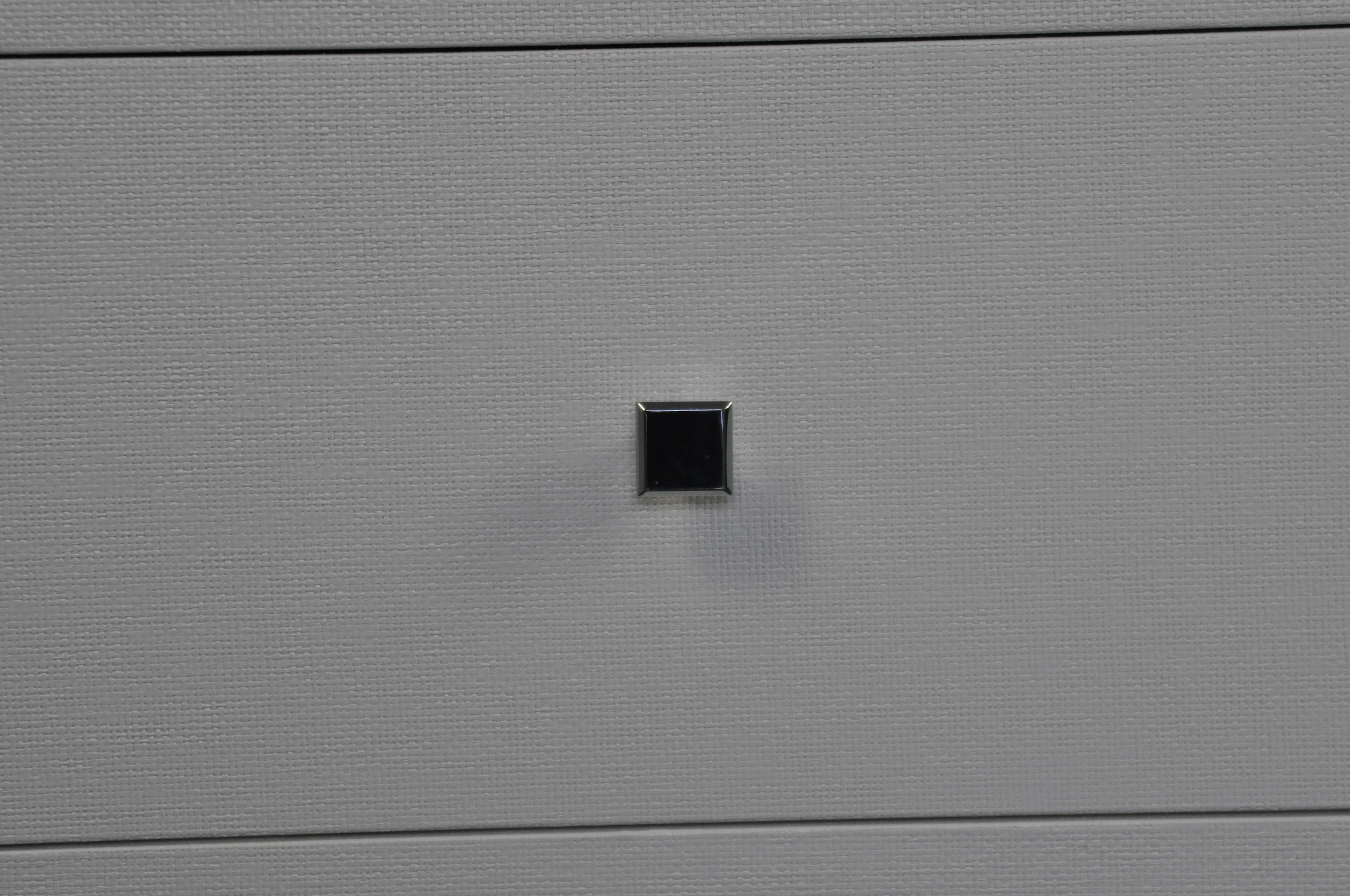 A six-drawer dresser with a white lacquered finish and chrome handles, set against a gray backdrop.