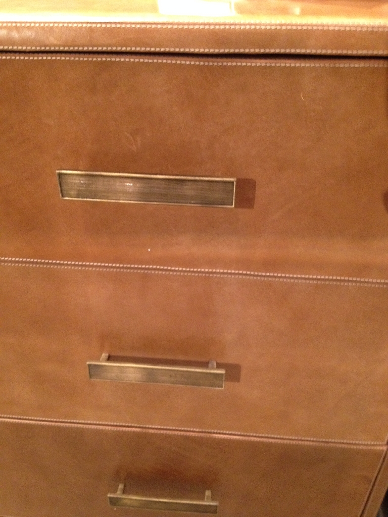Brown leather dresser with three drawers, curved edges, and antiqued gold metal feet.