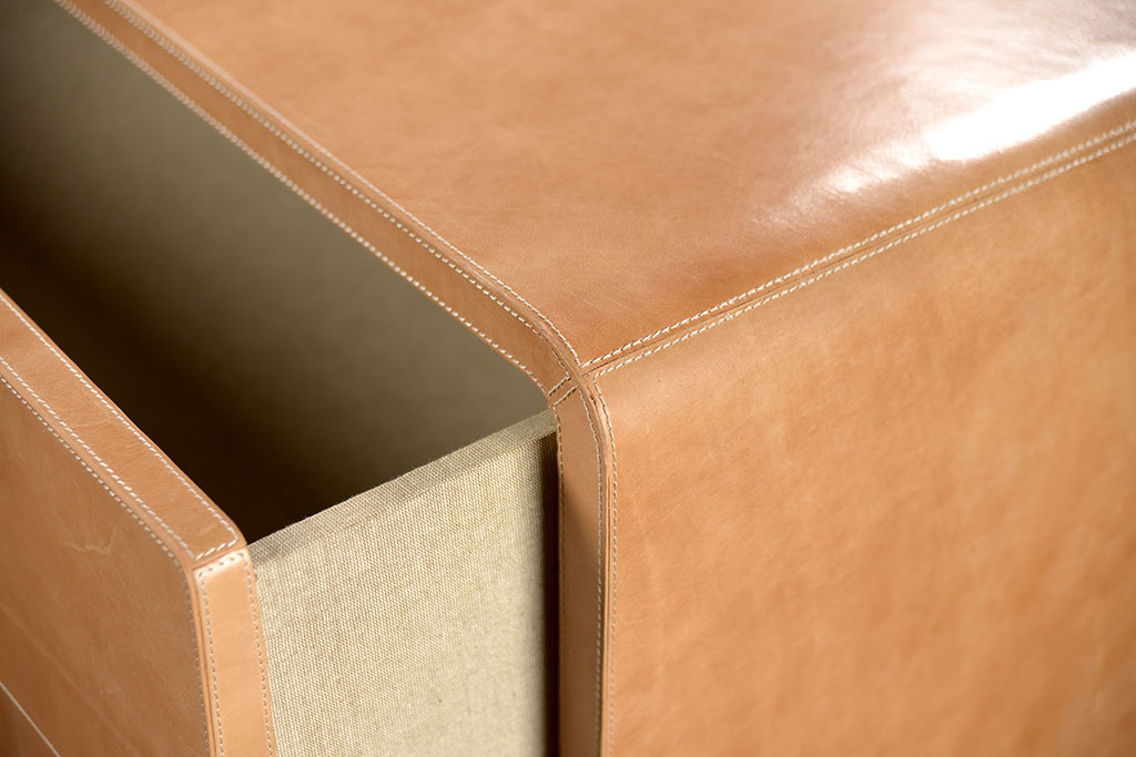 Brown leather dresser with curved edges and a distressed finish featuring three drawers with an open bottom and linen interior set against