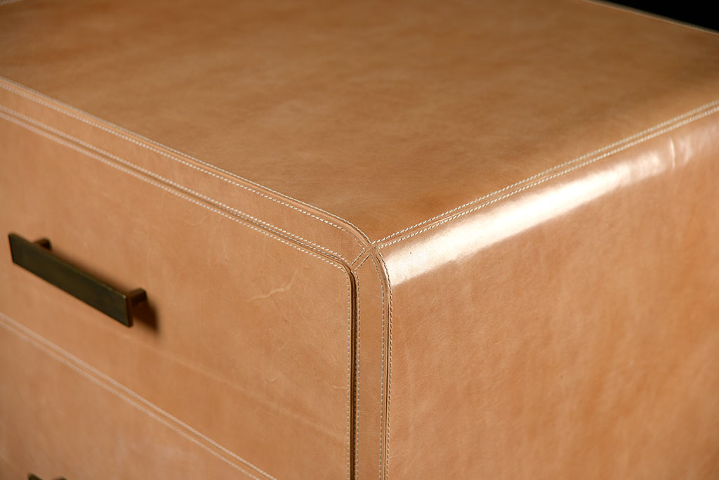Brown leather dresser with curved edges and three drawers featuring a rustic appearance with visible distressing and natural variations in color and