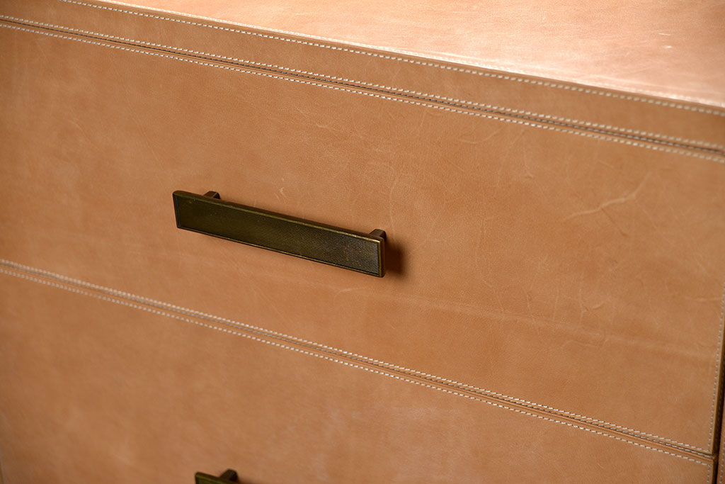 Brown leather dresser with curved edges and three drawers one of which is open revealing a linen interior The dresser has antiqued