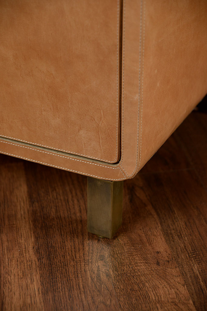 Brown leather dresser with curved edges and gold metal feet, showcasing its rustic texture and natural variations in color and grain.