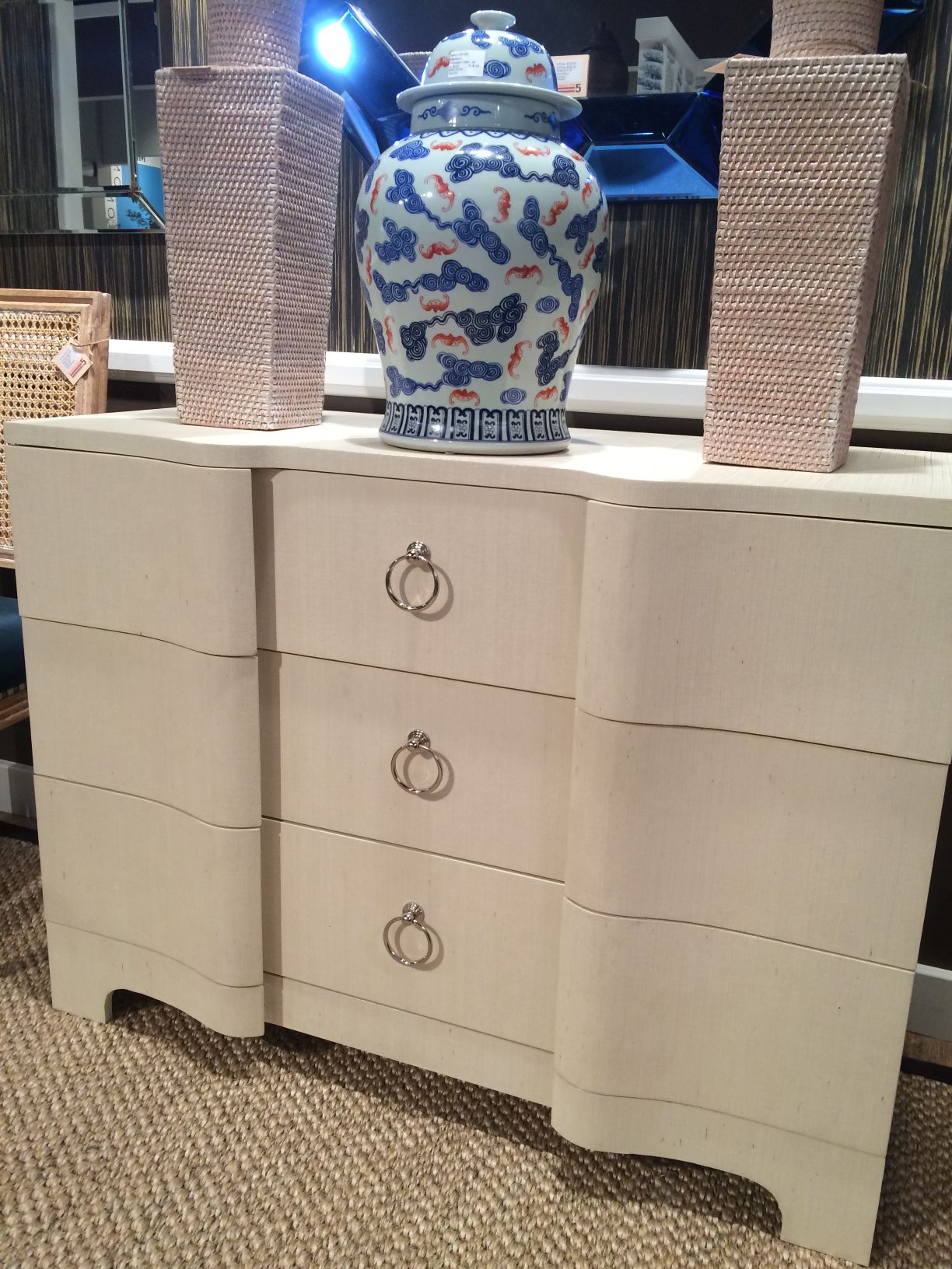 A large, beige dresser with a grasscloth finish and silver ring pulls, displayed in an interior setting.