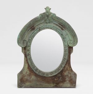 The image displays a large, oval-shaped mirror with an intricate design and a verdigris finish. It is set against a plain background.