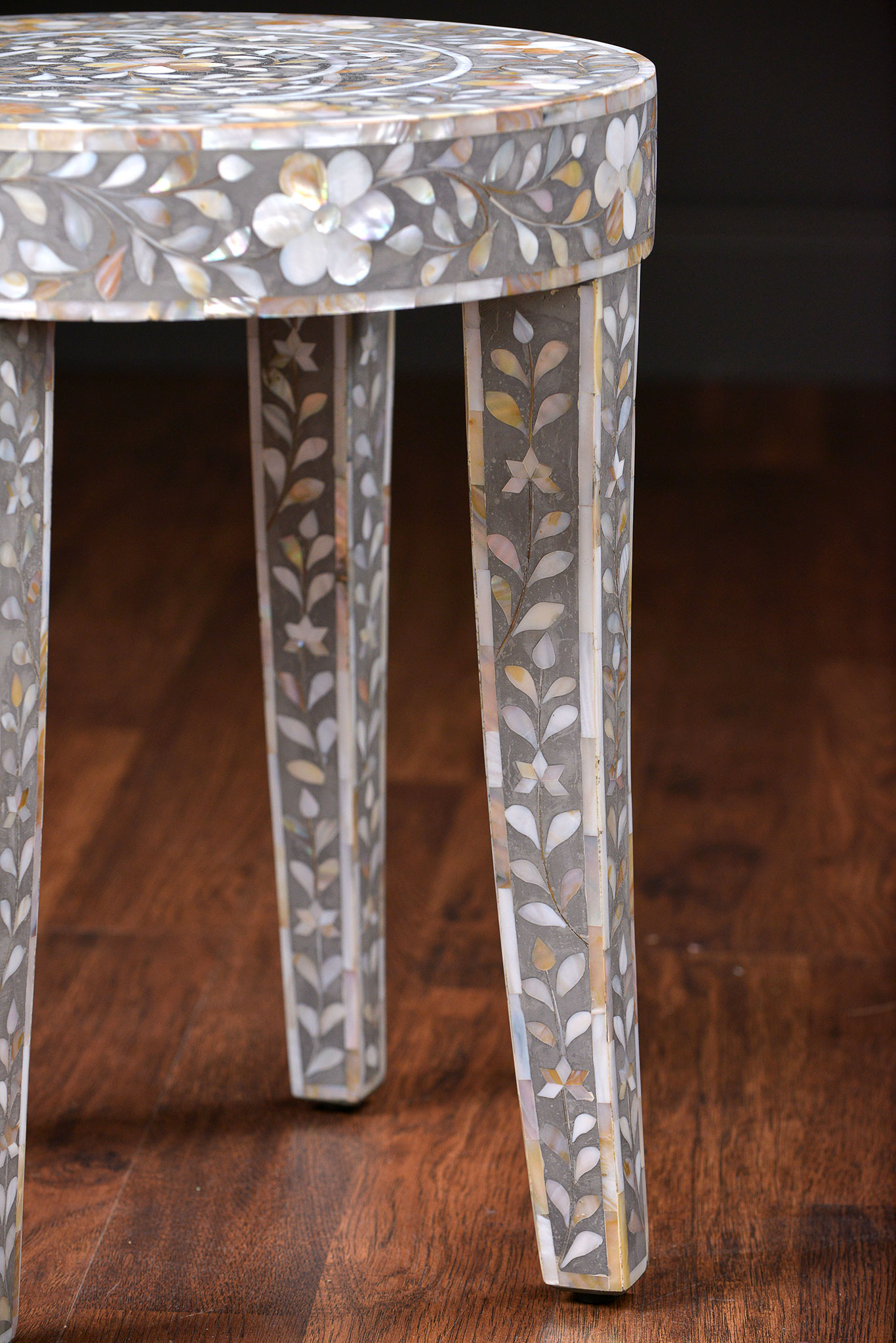 A decorative side table with a unique design featuring an inlaid mother of pearl top on a wooden base The table is