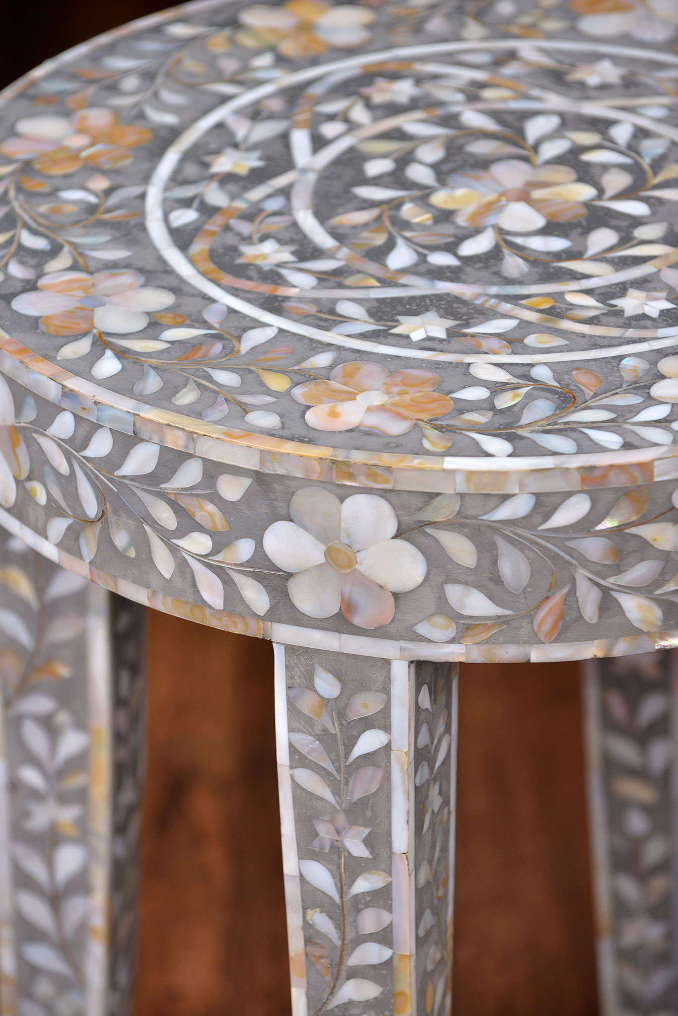 A decorative side table with intricate mother of pearl inlay on a grey resin base, featuring floral patterns and a round top.