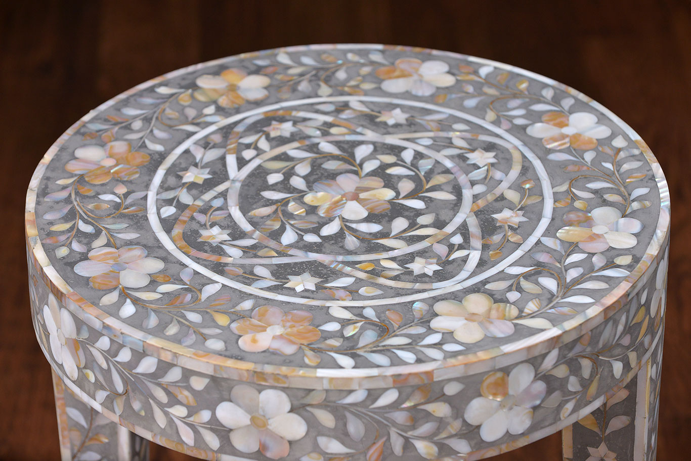 The image is a photograph of a decorative side table with an intricate design It features a top adorned with a pattern